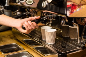 Barista making fresh takeaway coffee. Close-up view on hands with portafilter, barista coffee preparation service concept.